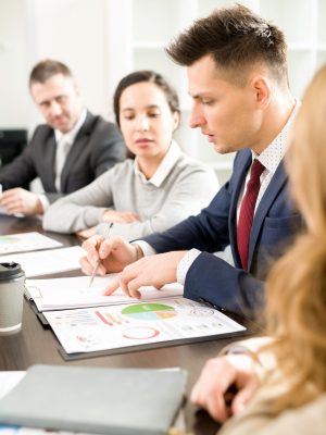 Serious concentrated business analyst viewing report while discussing strategy with colleagues at meeting