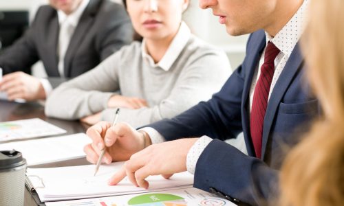 Serious concentrated business analyst viewing report while discussing strategy with colleagues at meeting